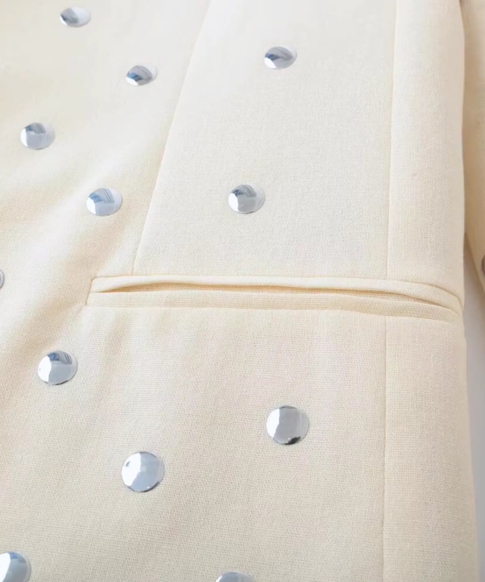 Close up of the silver studs on the pocket and sleeve of the beige blazer