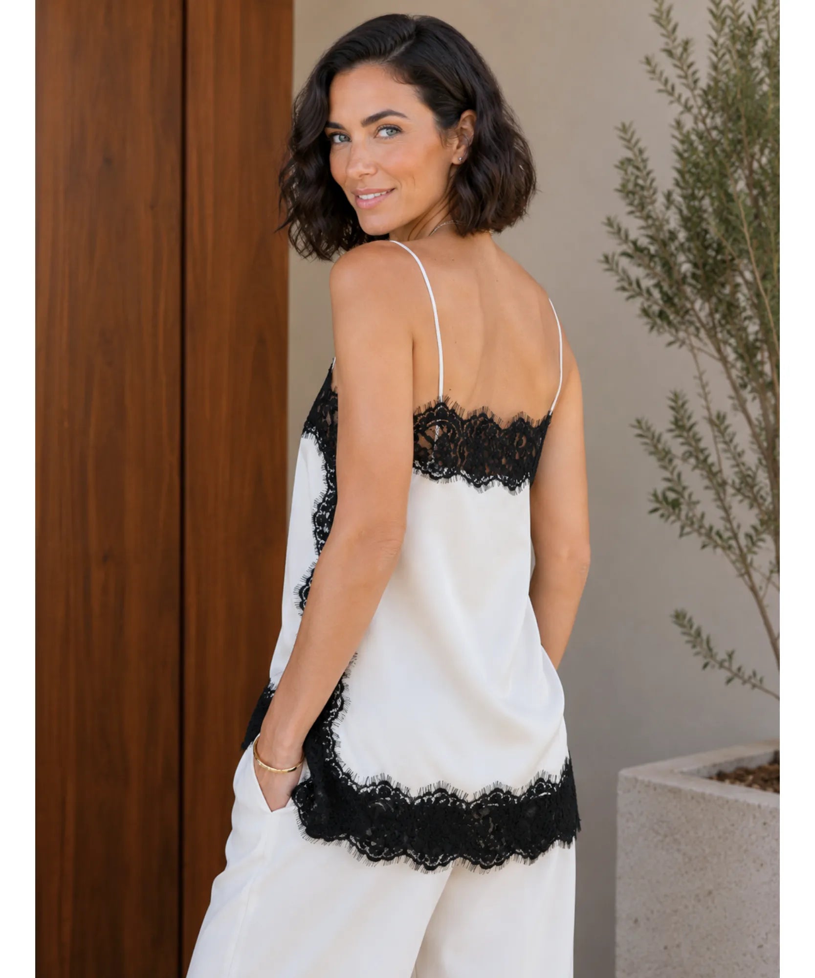 Back view of ivory satin cami top with black lace styled with white wide-leg trousers