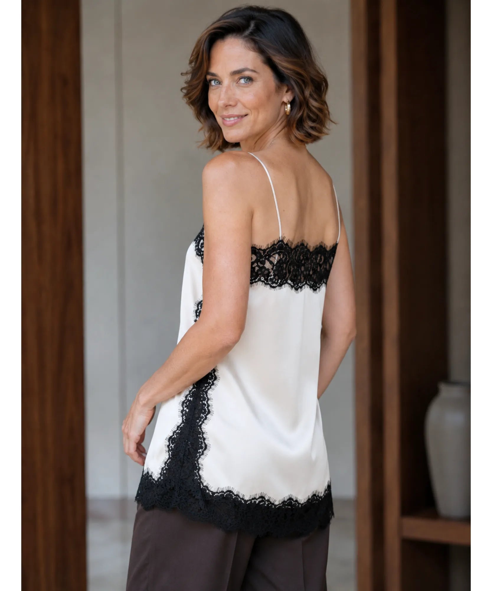 Back view of ivory satin cami top with black lace trim and dark trousers
