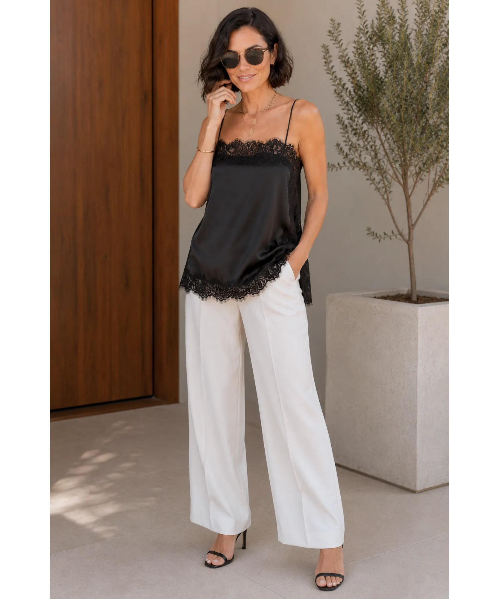 Black satin cami top with lace trim styled with white wide-leg trousers and sunglasses