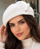 Woman wearing an ivory wool-blend French beret with a metal brooch