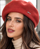 Woman wearing a red wool-blend French beret with a metal brooch
