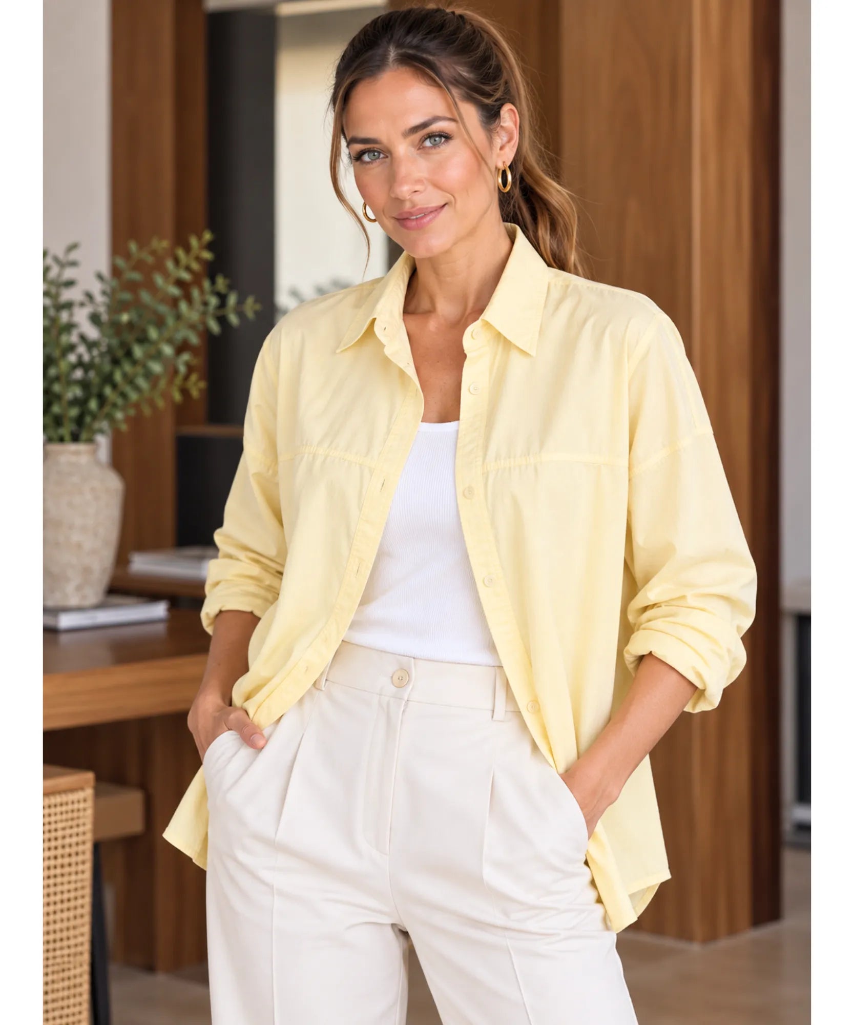 Women's long sleeve shirt in light yellow worn open over a white top with ivory trousers