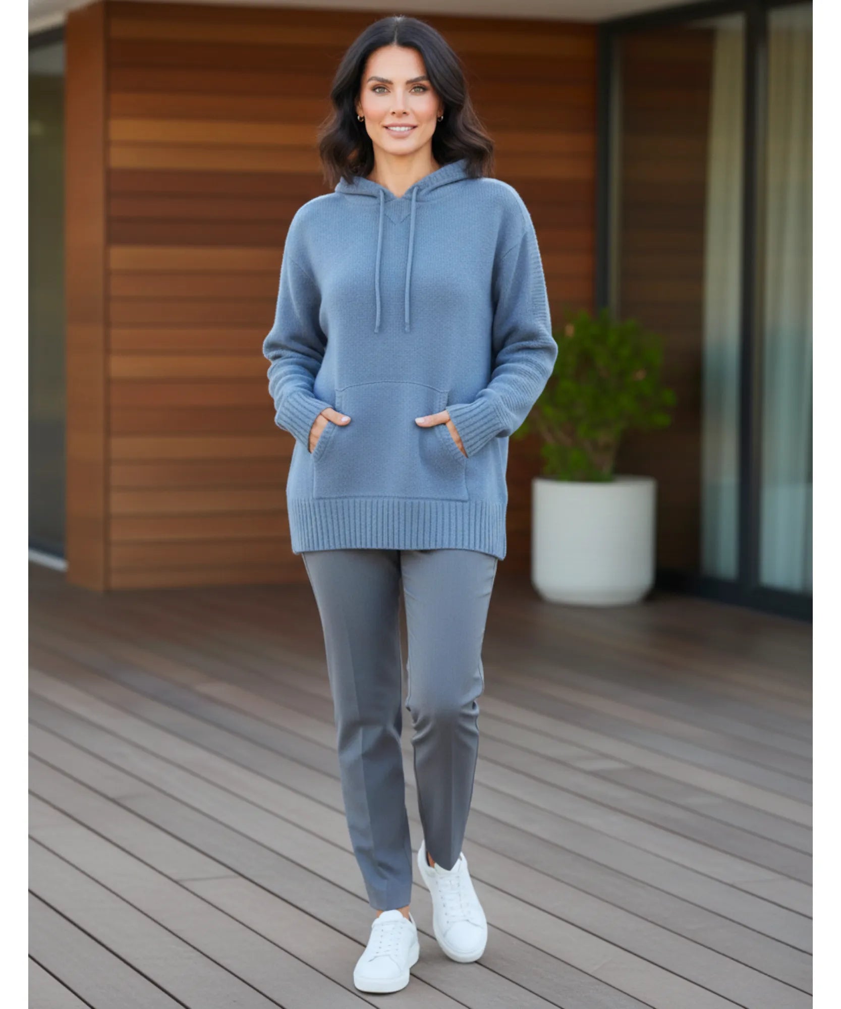 Women's dusty blue knit hooded sweater styled with grey pants and white sneakers