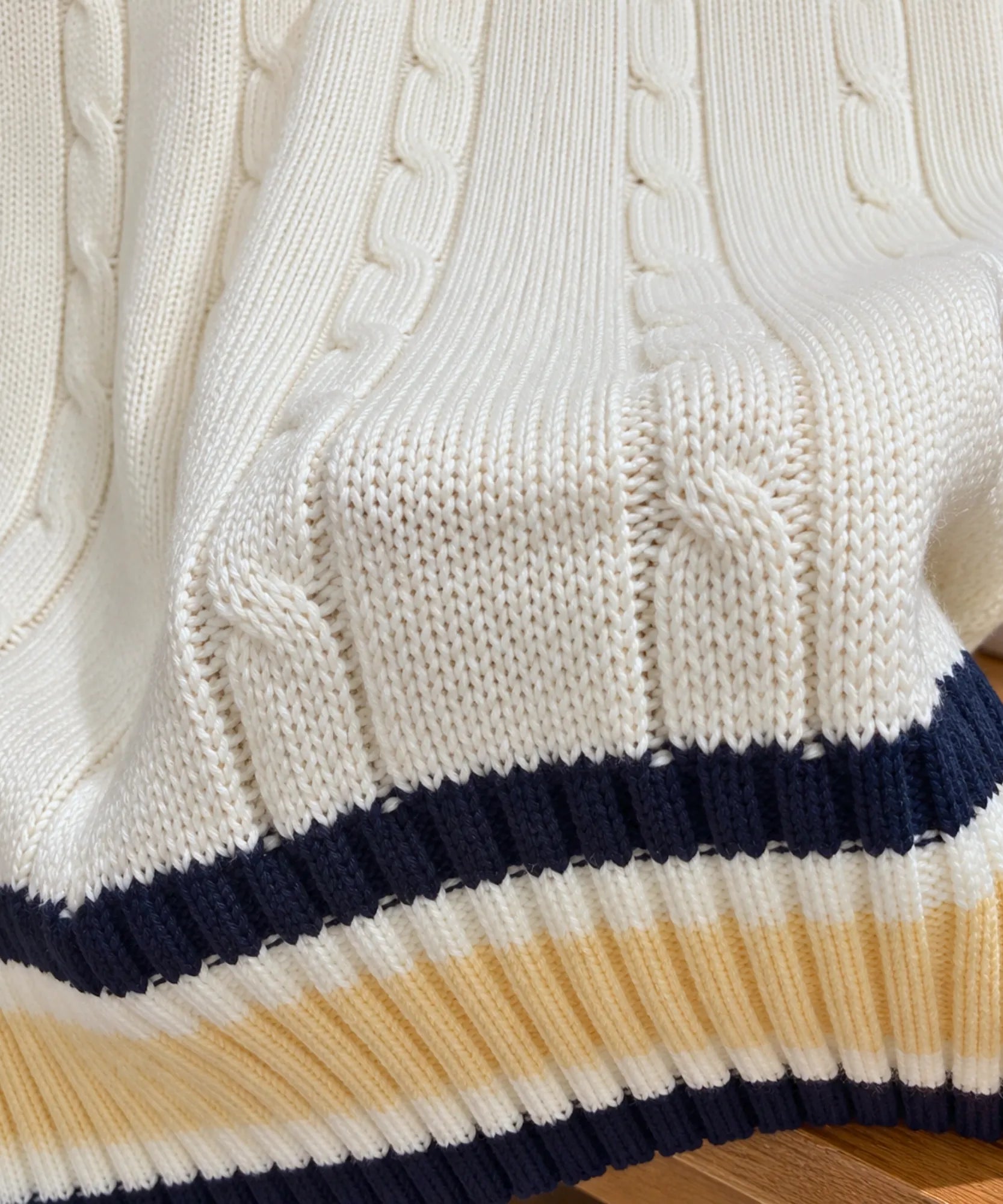 Close-up of the cable knit texture and ribbed striped hem of an ivory sweater vest