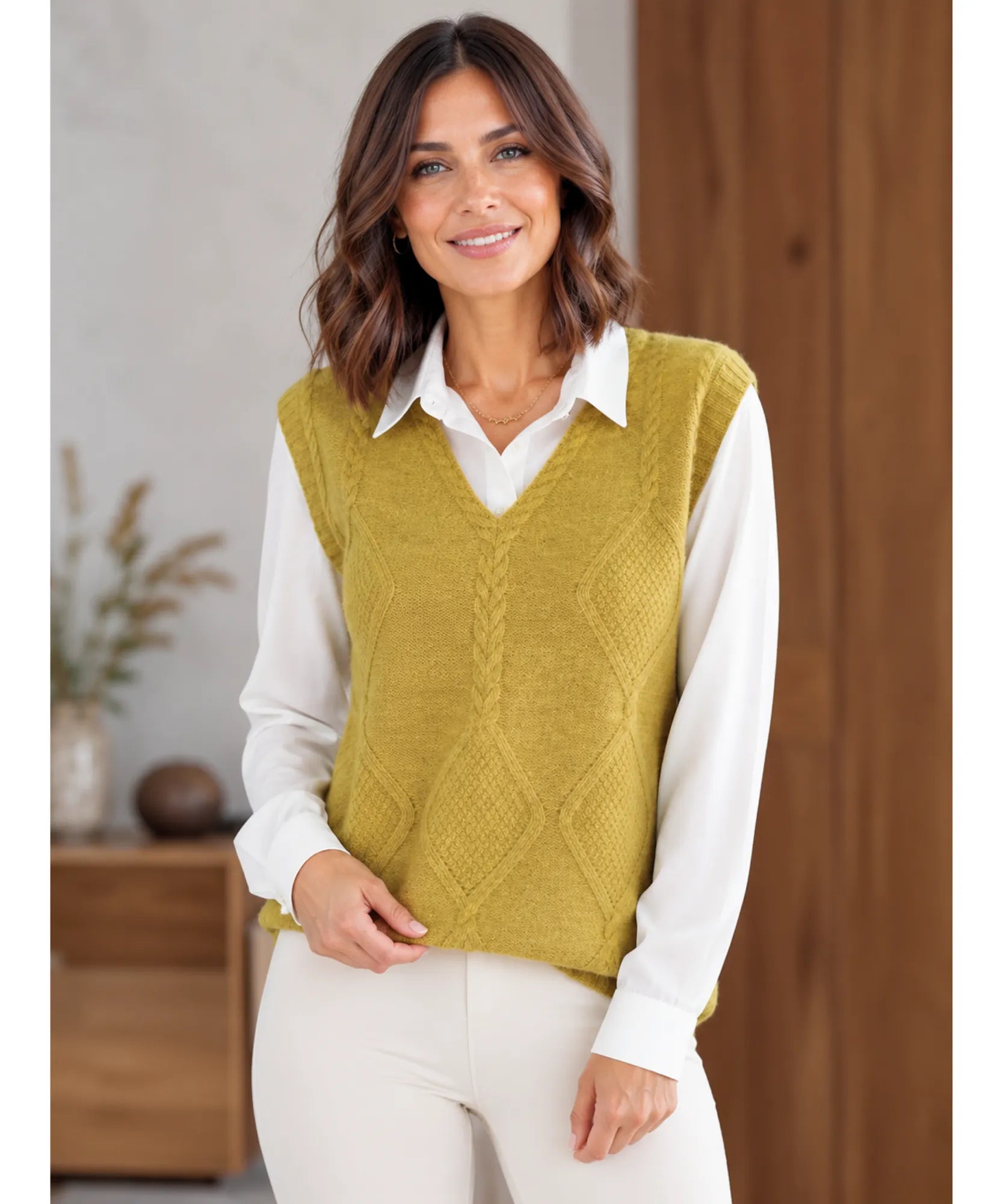Women's cable knit V-neck sweater vest in mustard, layered over a white shirt