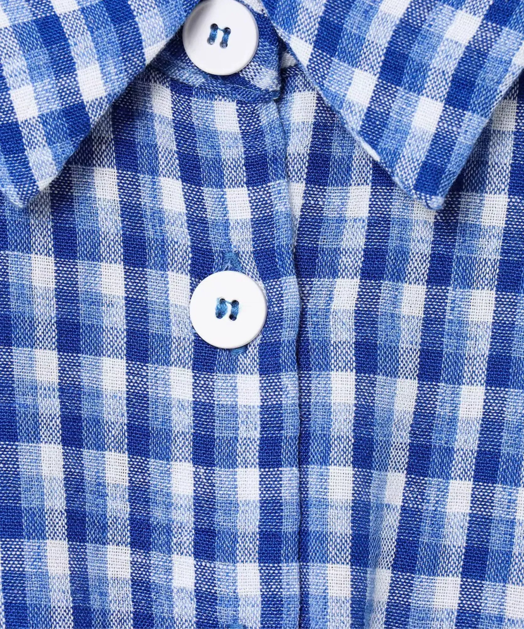 Fabric close up of blue and white gingham romper with white buttons