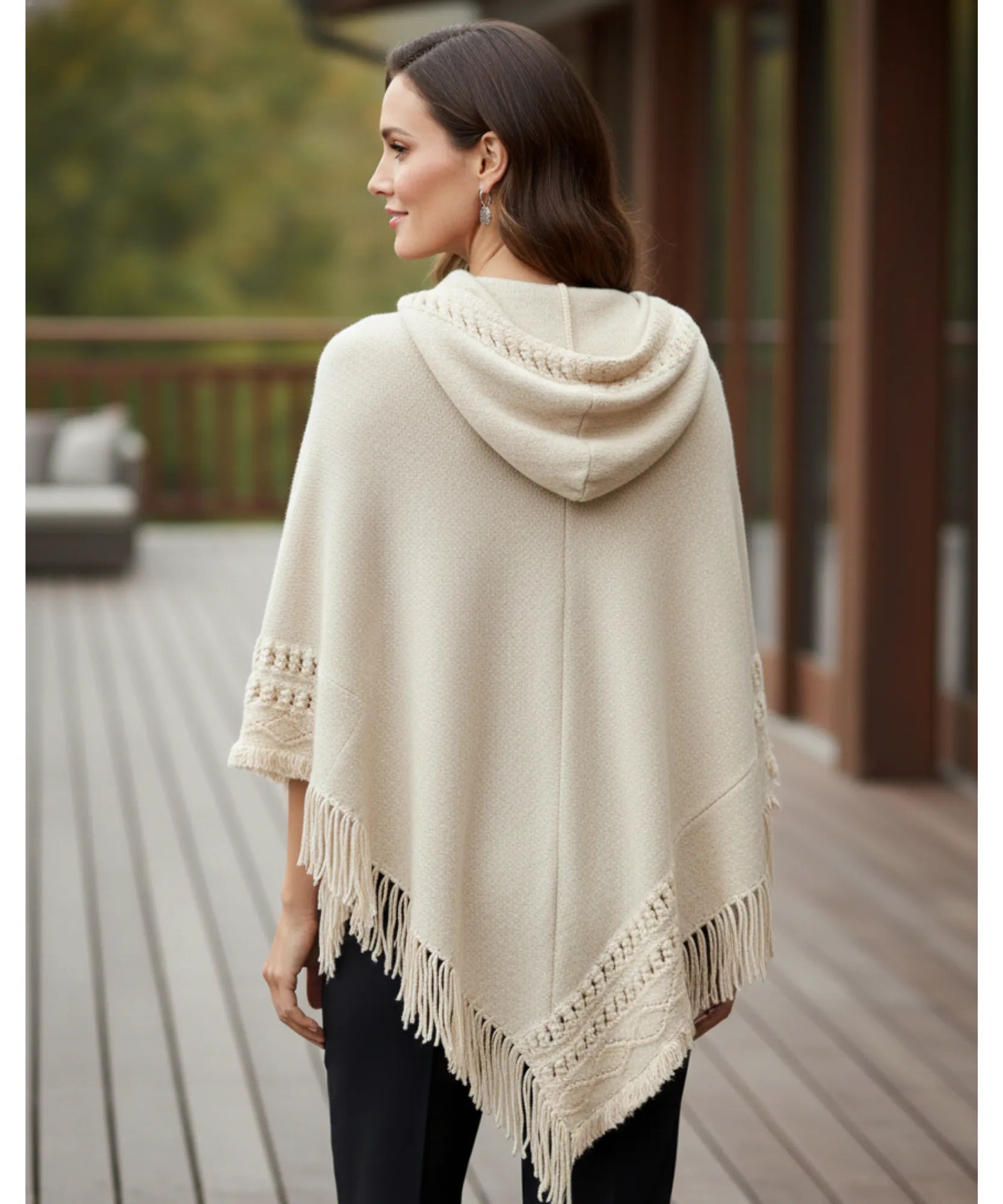 Women's hooded poncho sweater in ivory chunky knit, back view on outdoor deck