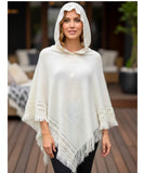 Women's hooded poncho sweater in white chunky knit with fringe trim, styled with black leggings