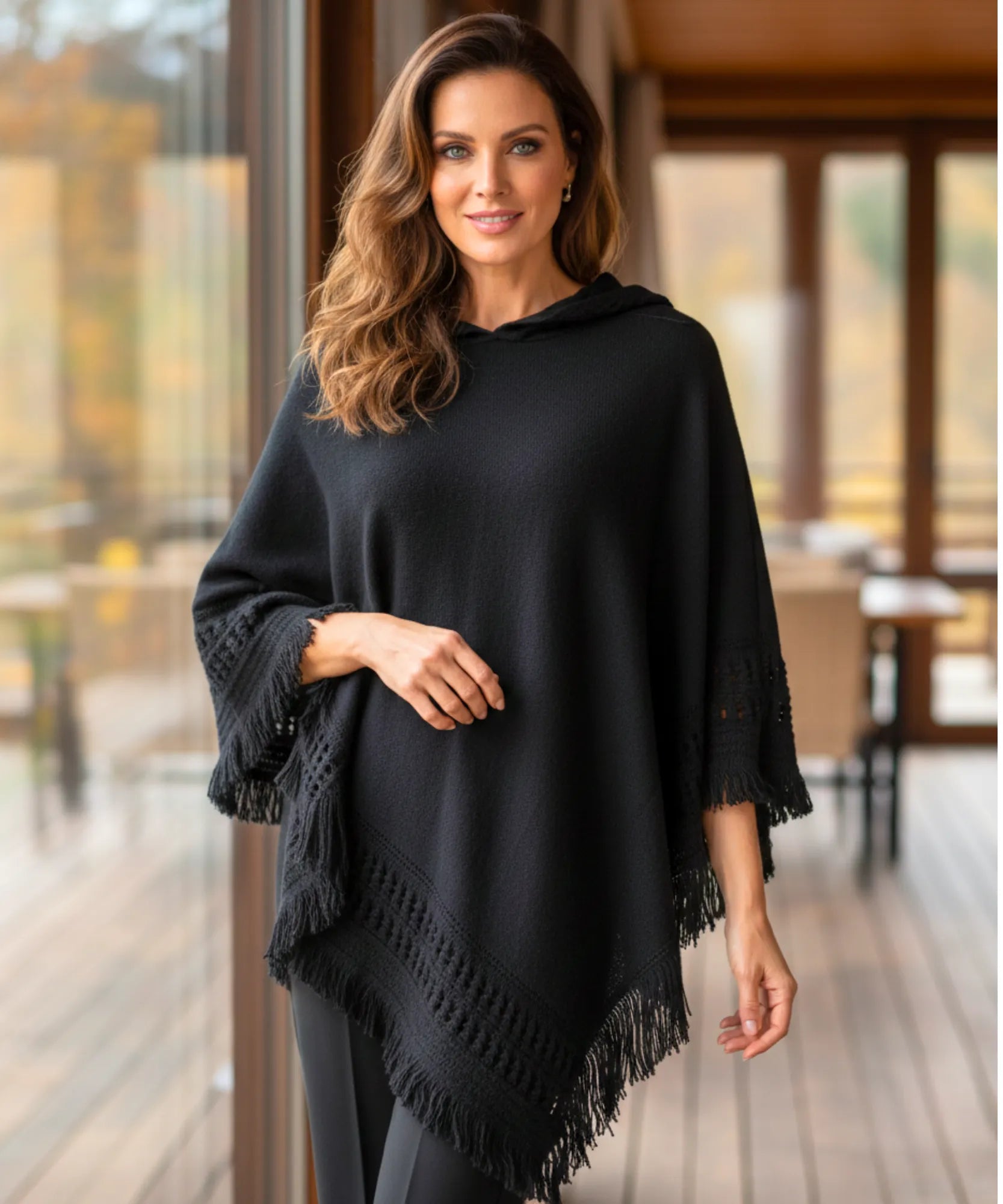 Women's hooded poncho sweater in black chunky knit with fringe trim, front view