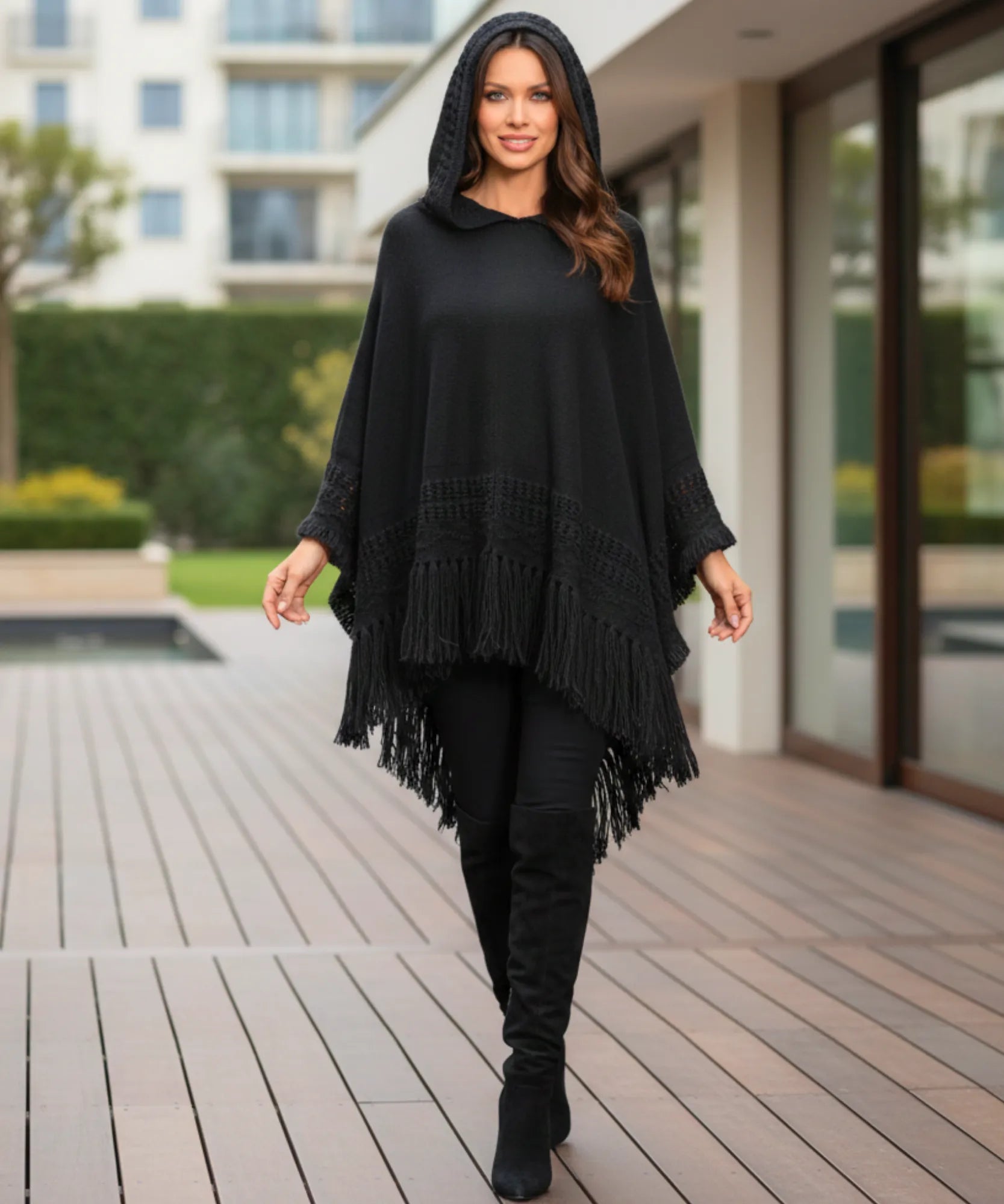 Women's hooded poncho sweater in black chunky knit, back view showing fringe hem