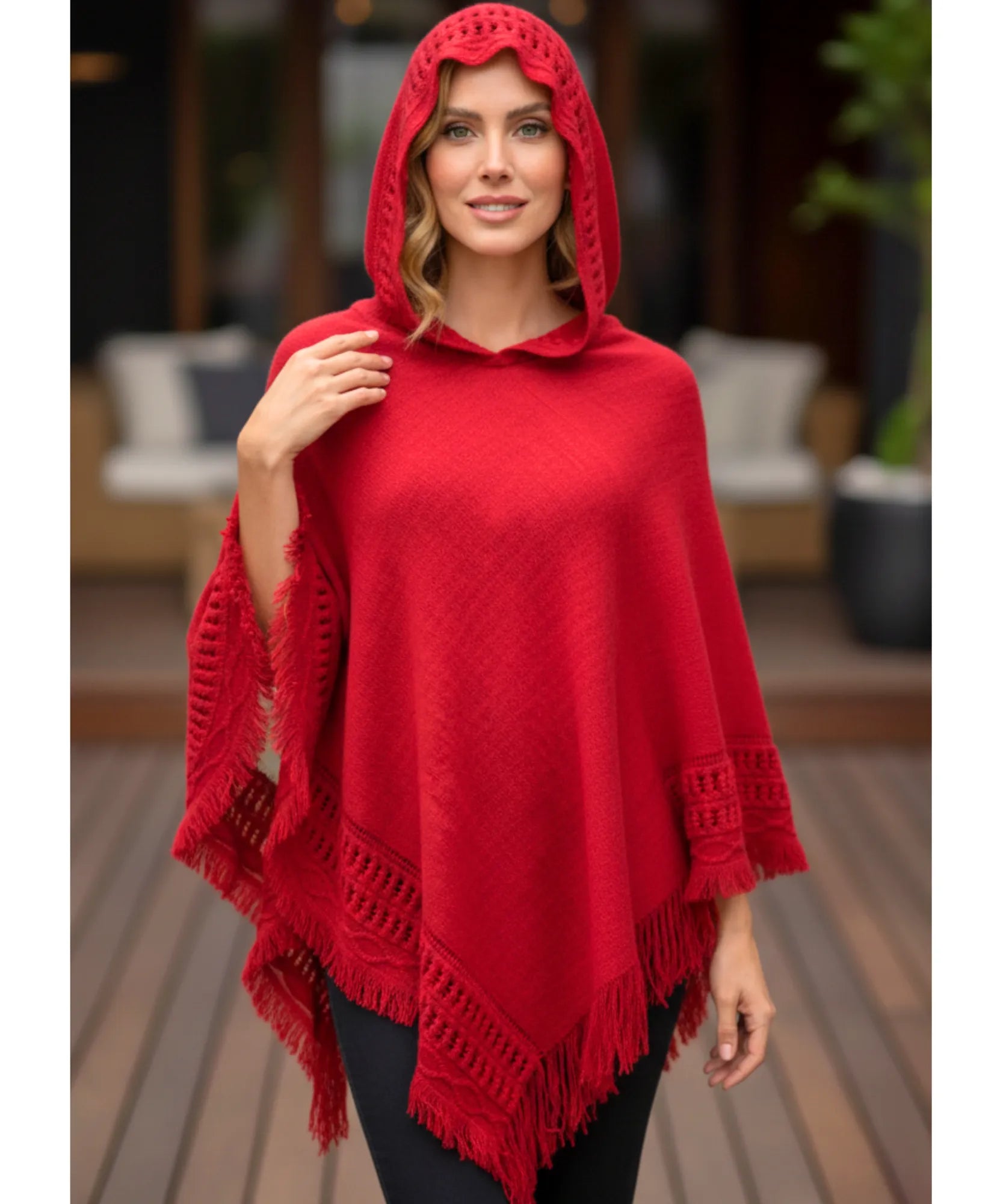 Women's hooded poncho sweater in red chunky knit with fringe trim, hood up