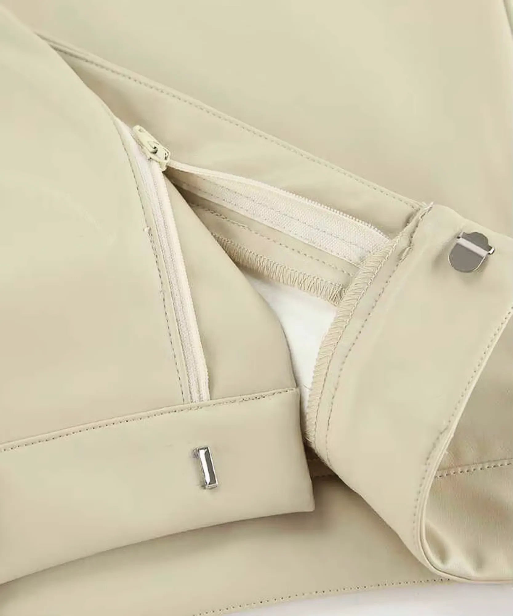 Detail of the hidden side zip and metal button on an ivory vegan leather skirt